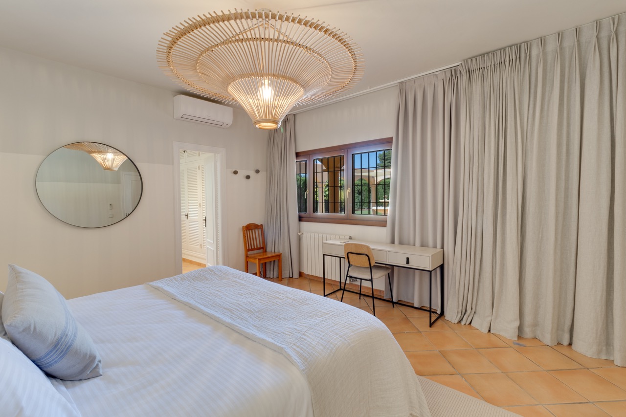 Dormitorio con cama doble, espejo redondo y cortinas hasta el suelo