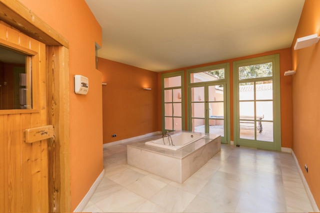 Bathroom with bathtub, marble flooring and doorway to wooden sauna