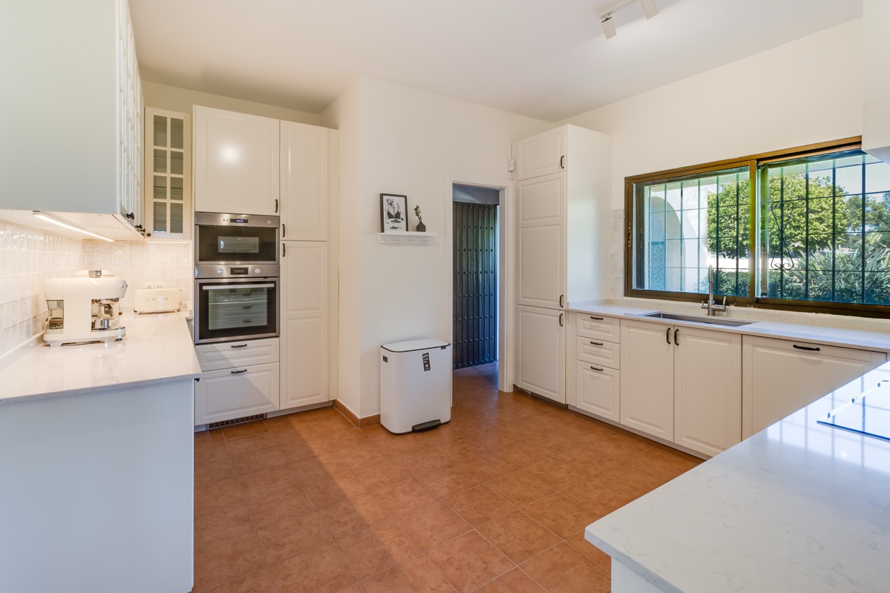 Cocina con muebles blancos, electrodomésticos integrados y ventana al jardín
