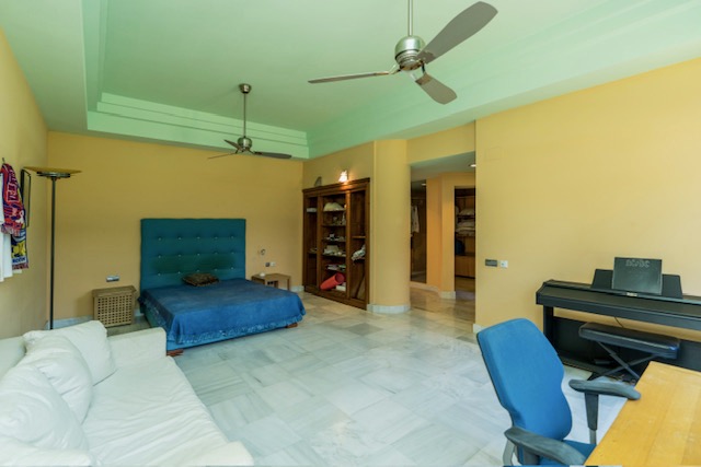 Bedroom or sitting room with blue sofa, yellow walls and tiled flooring