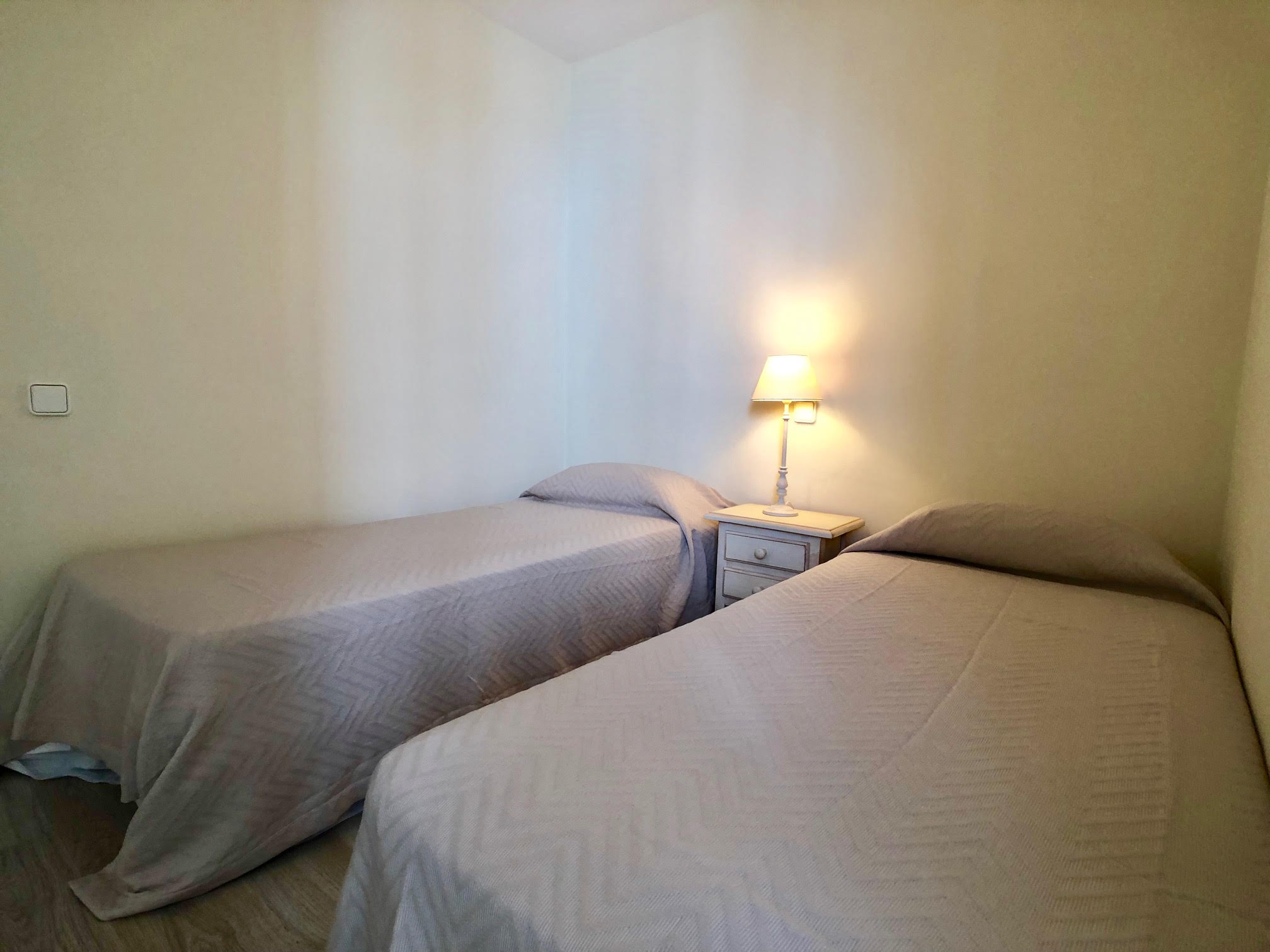Dormitorio con dos camas individuales, lámpara de noche y luz natural suave