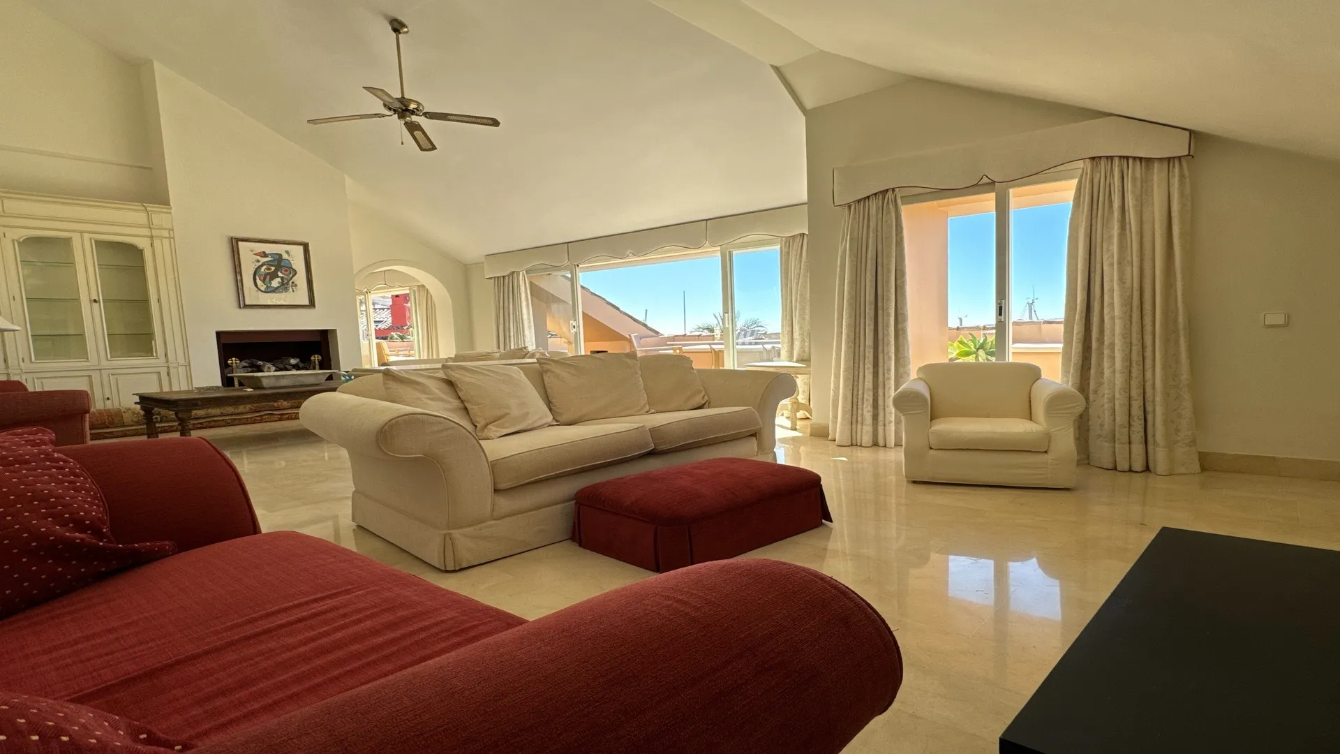Salón con sofás rojos, ventanas grandes y vistas al puerto deportivo