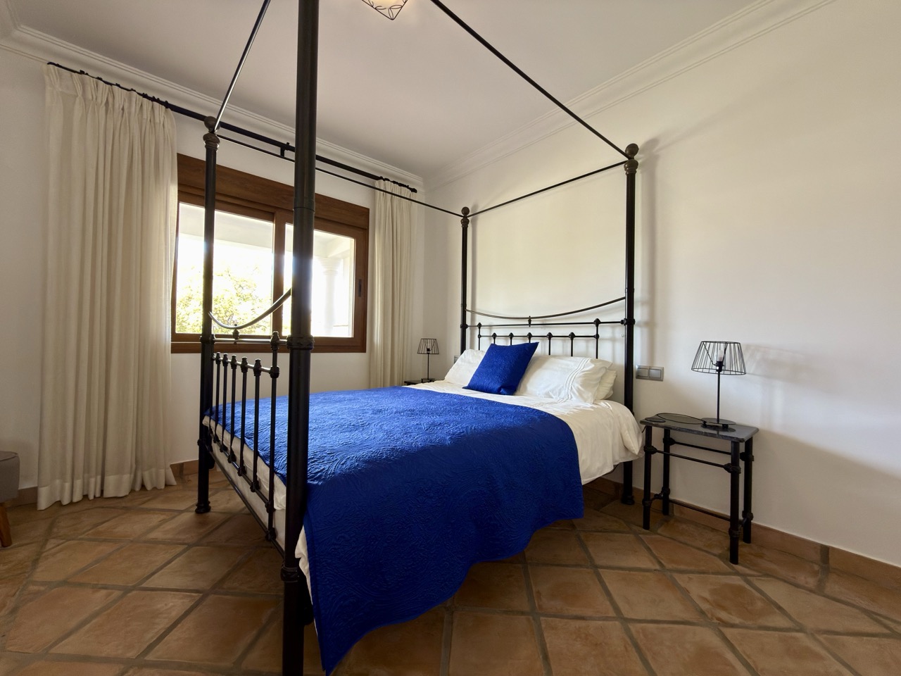 Bedroom with blue bed, canopy frame and terracotta flooring