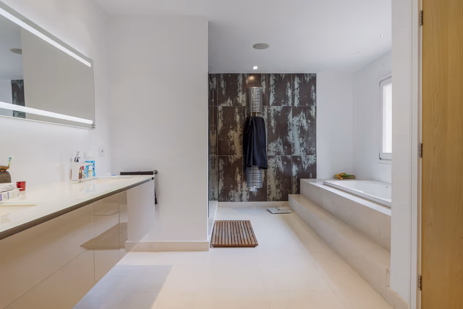 Bathroom with long vanity, mirror lighting and textured shower wall