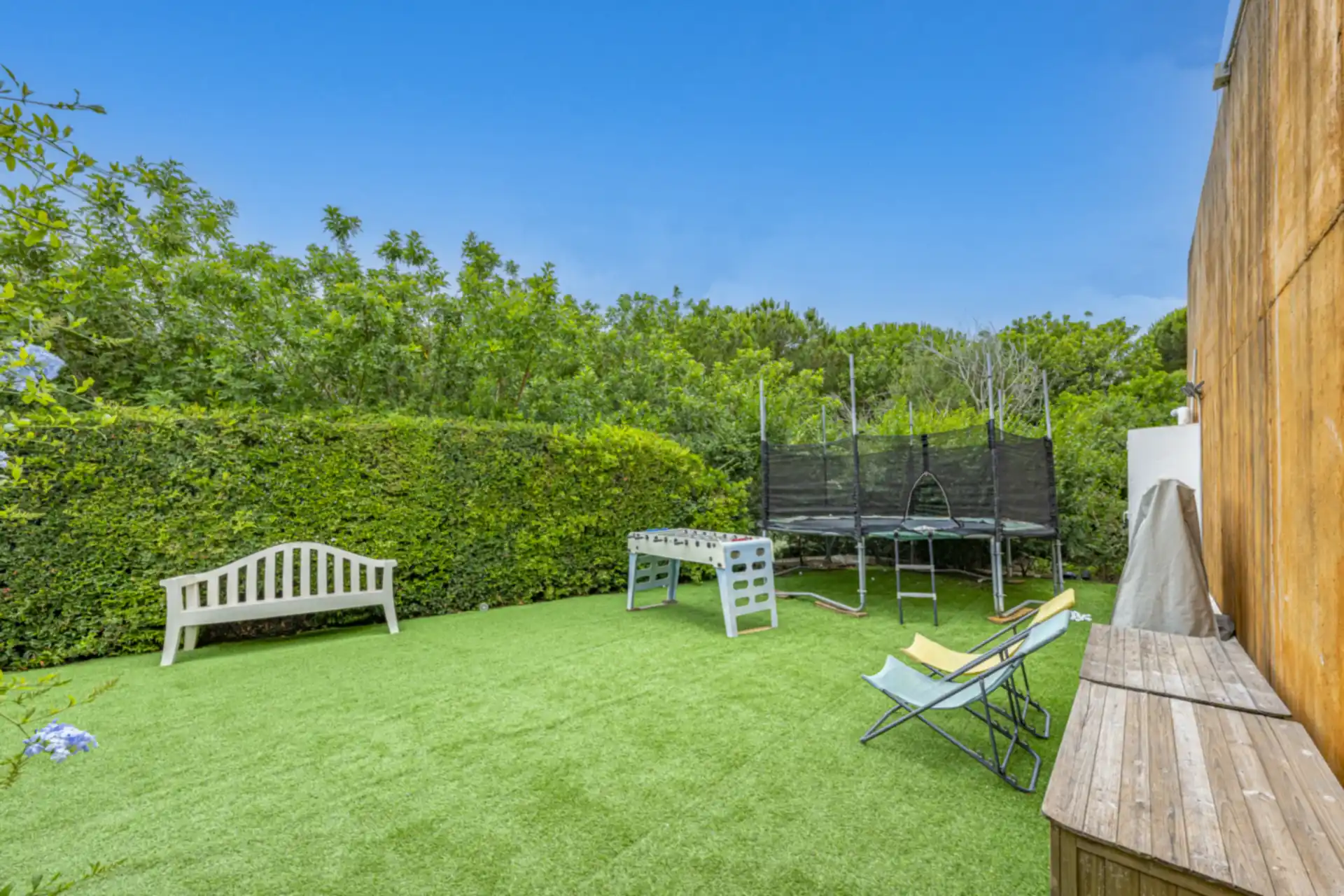 Garden play area with trampoline and table football, enclosed by hedges