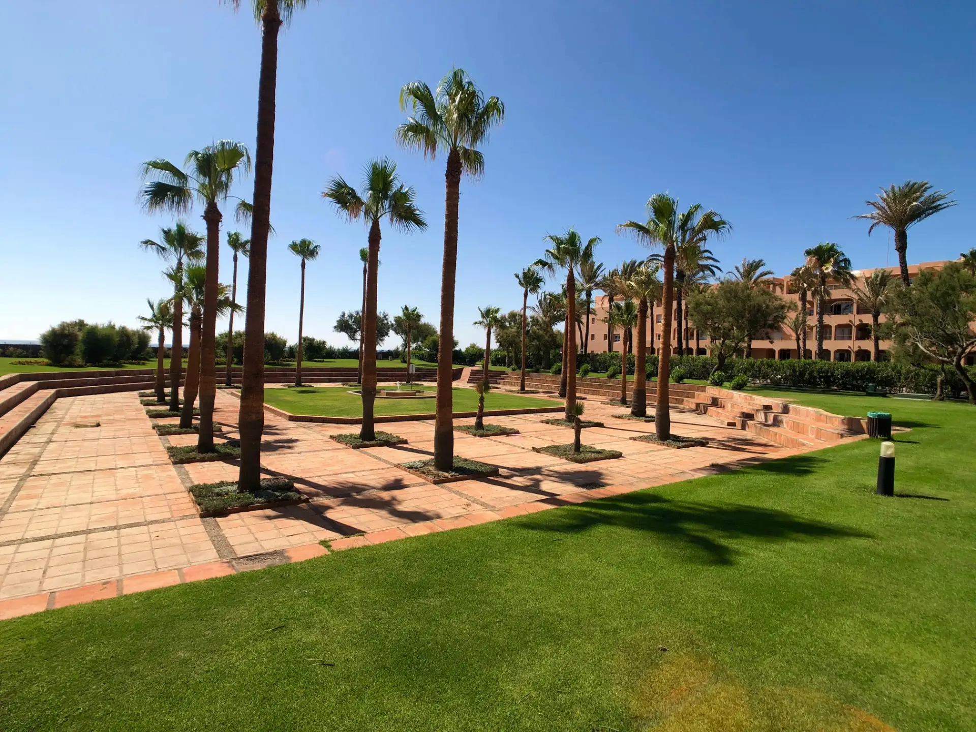 Camino del jardín con palmeras, césped y entorno de apartamentos en primera línea de playa
