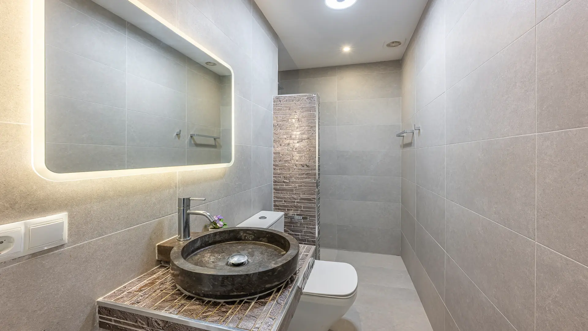 Baño de invitados con lavabo redondo, pared texturizada y espejo iluminado