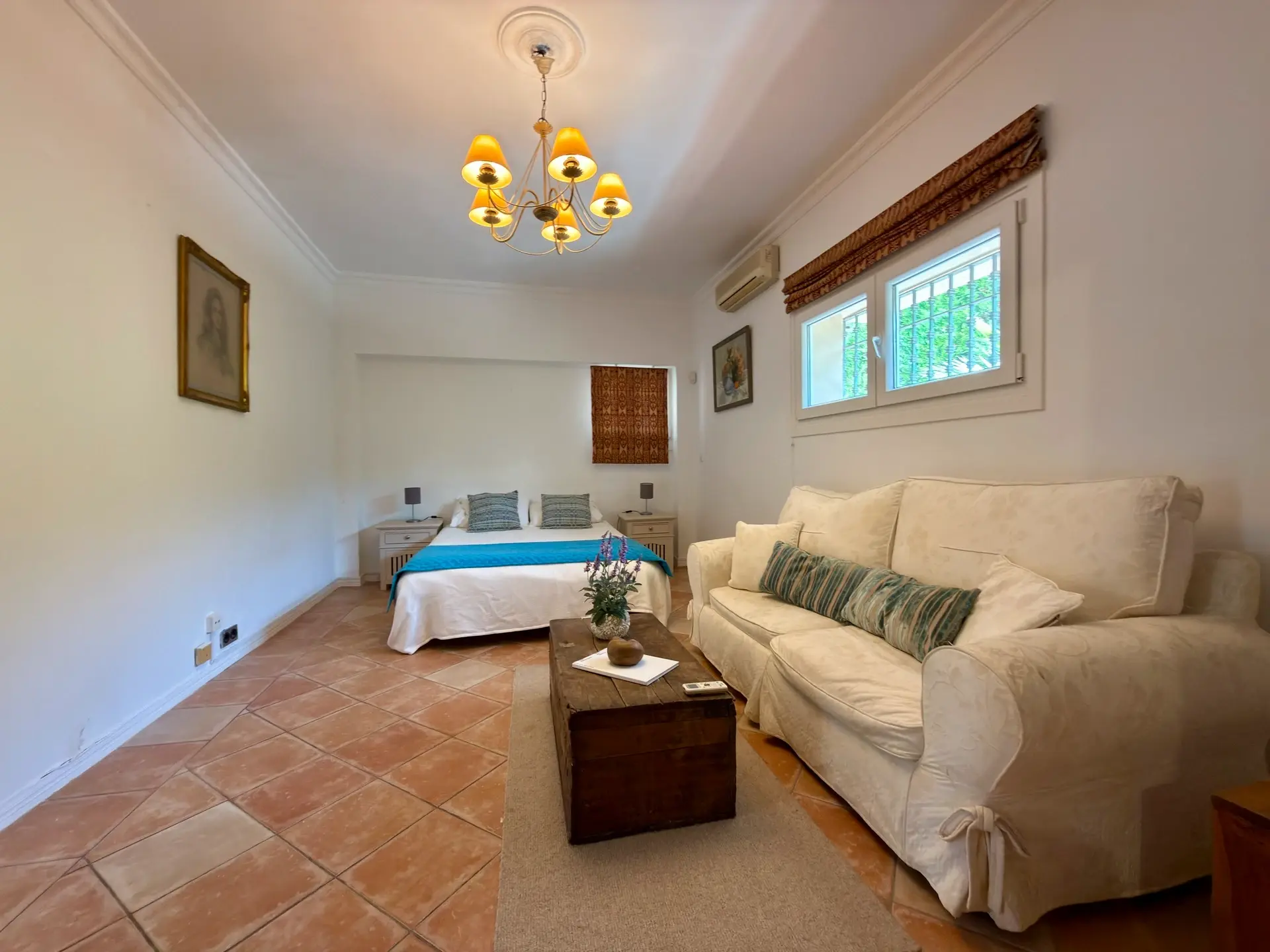 Bedroom with sofa seating, chandelier and terracotta flooring