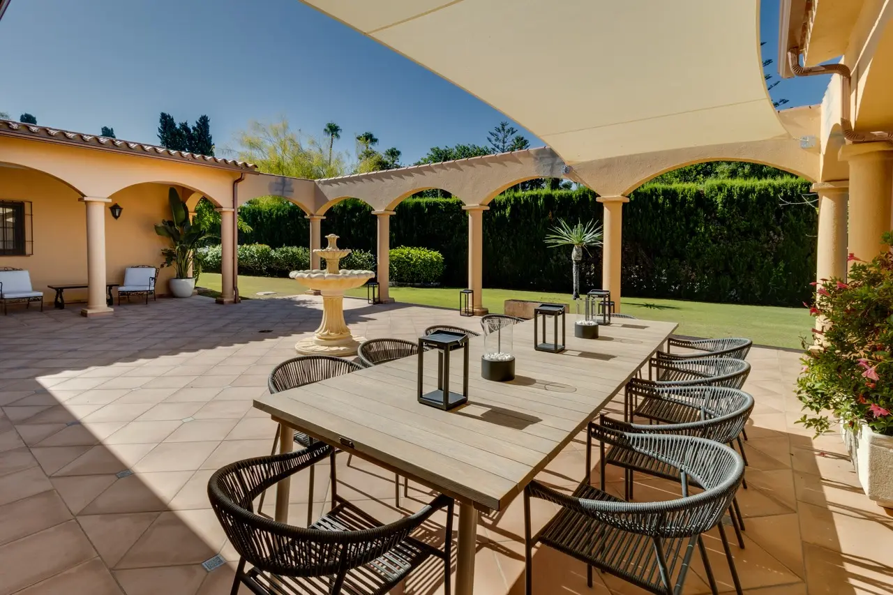 Terraza exterior cubierta con comedor, arcos y vistas al jardín