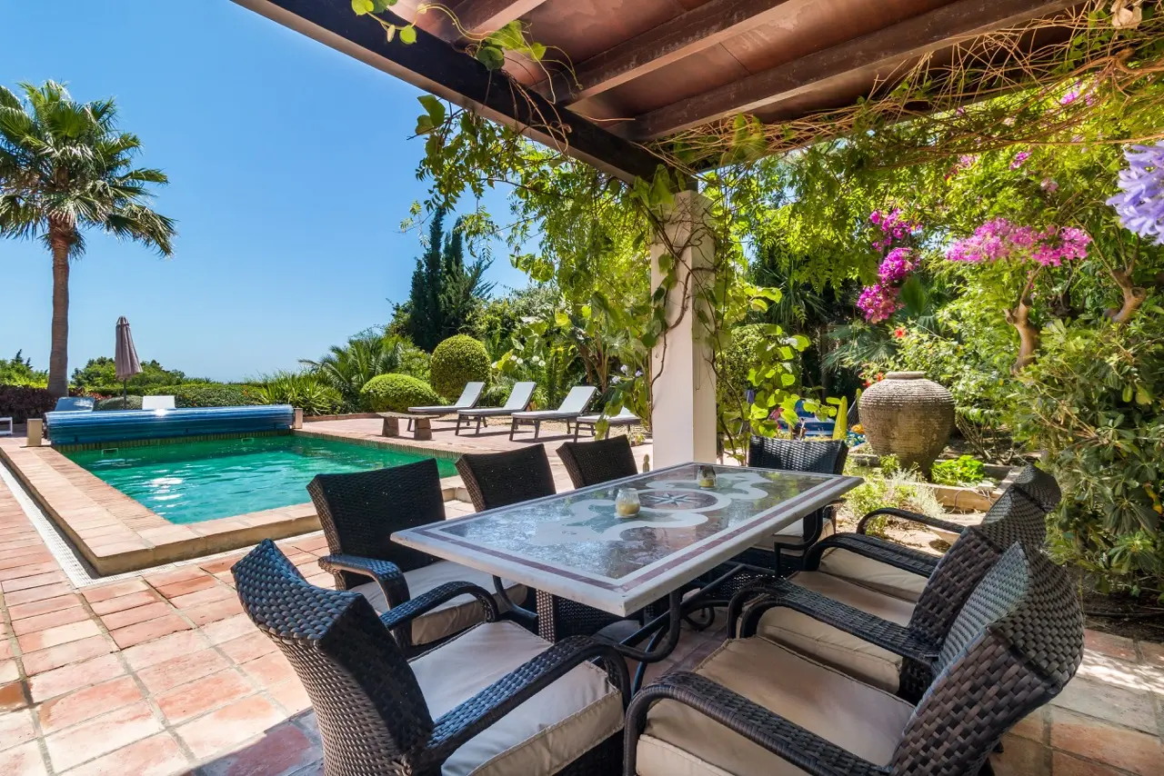 Terraza cubierta con asientos exteriores, piscina y vistas al jardín
