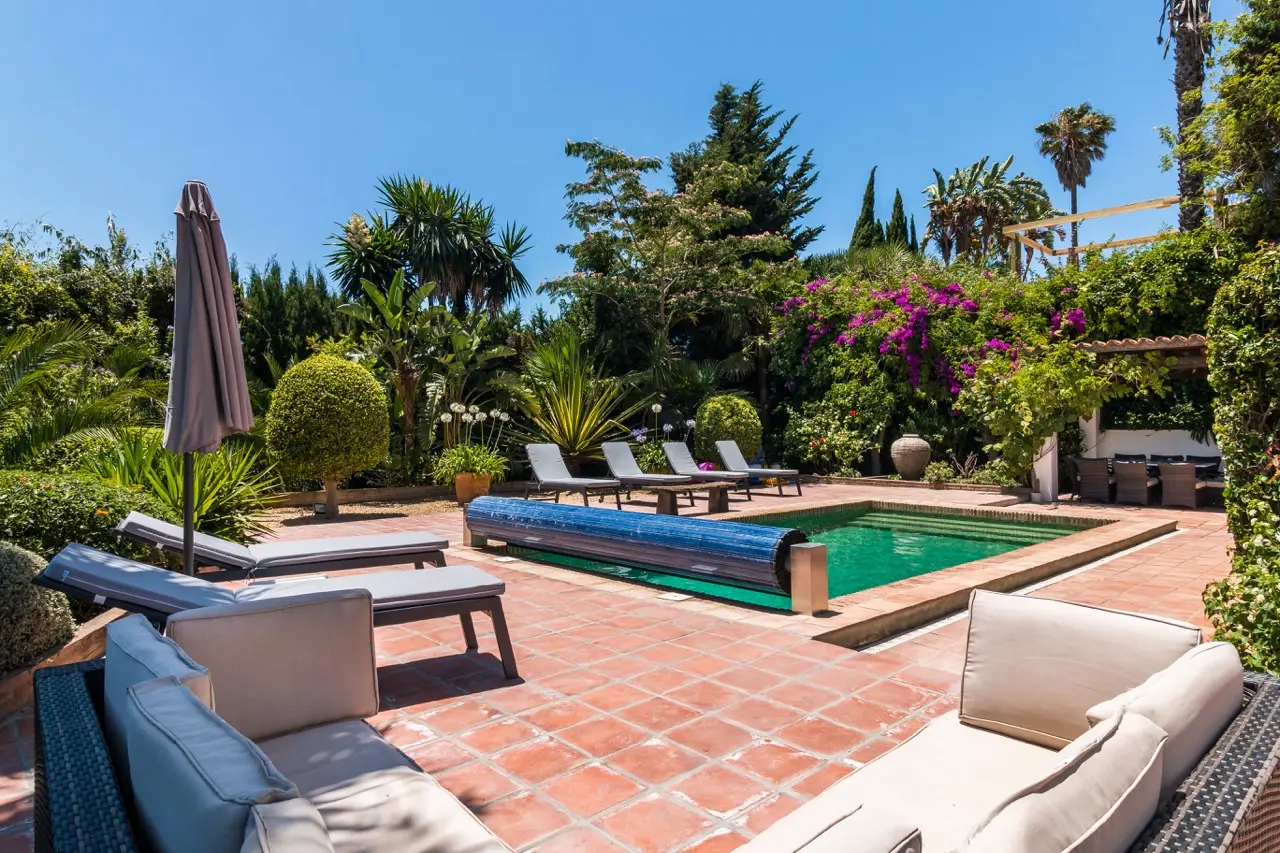 Terraza de la piscina con asientos exteriores, tumbonas y jardín paisajístico