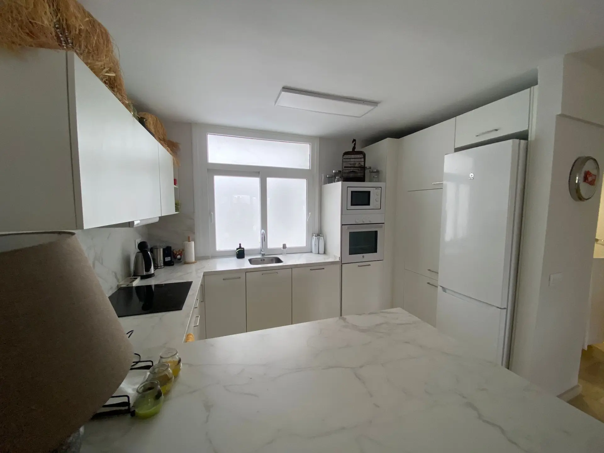 Cocina con muebles blancos, barra de desayuno y luz natural