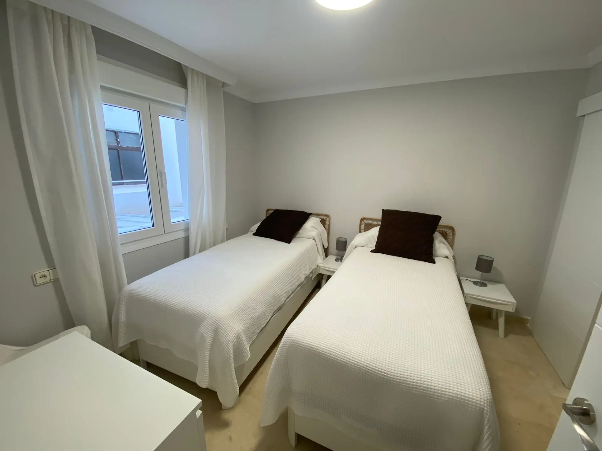 Dormitorio con dos camas individuales, paredes blancas y ventana