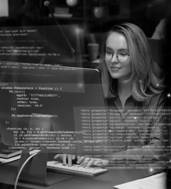 Woman with glasses typing on a desktop keyboard, overlaid with transparent lines of computer code.