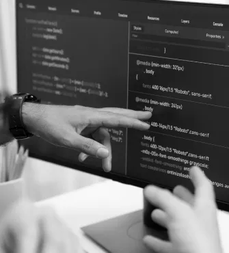 Two hands pointing and interacting with code displayed on a computer monitor.