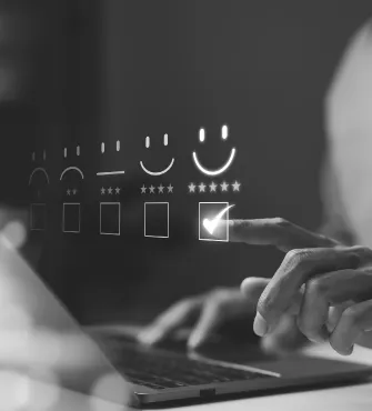 Person selecting a five-star happy face rating on a digital feedback interface over a laptop.