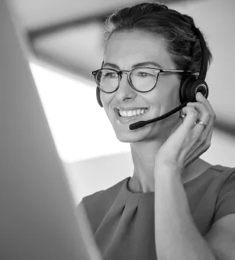 Smiling woman wearing glasses and a headset, working at a computer.