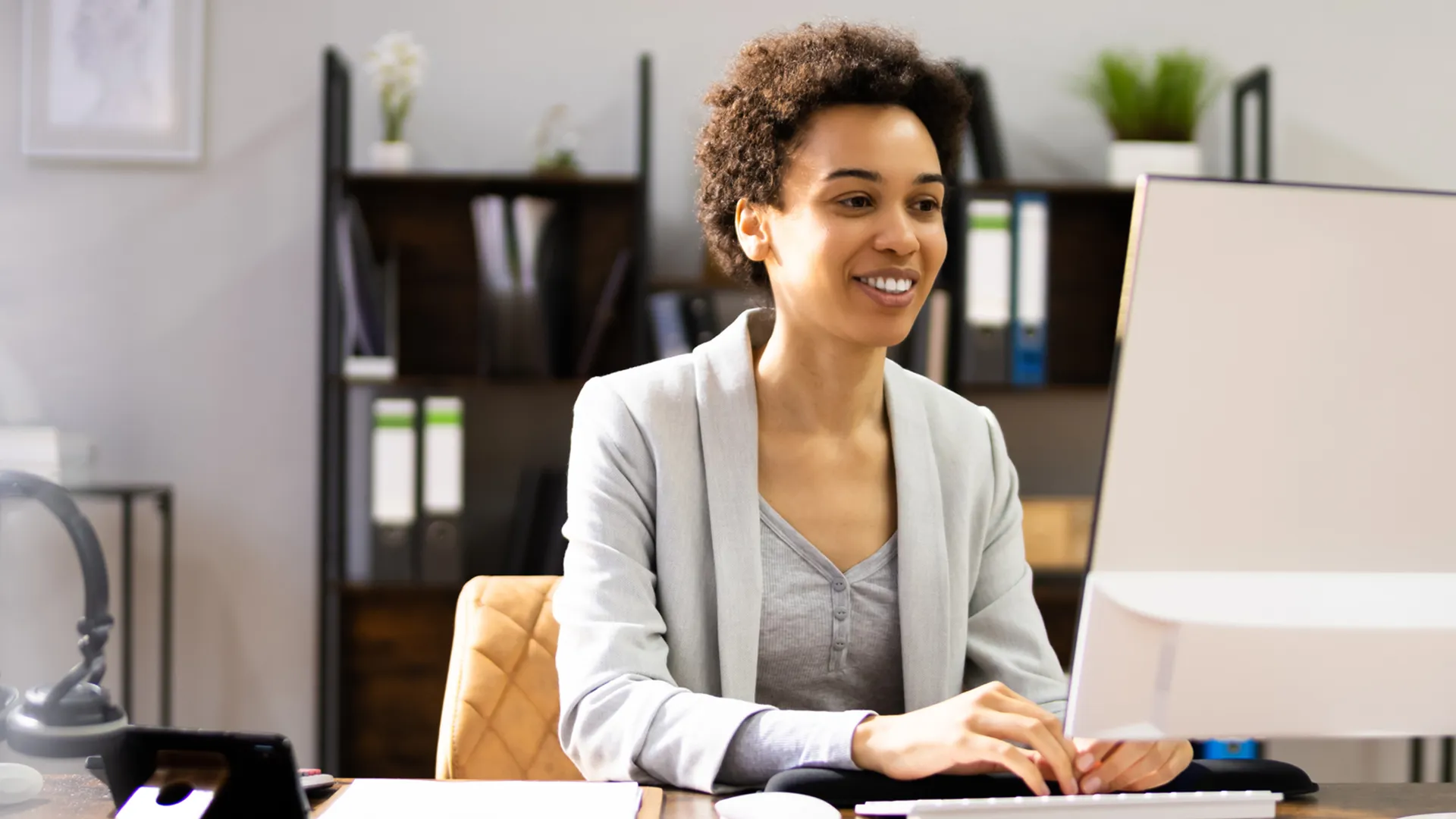 Smiling woman typing on a keyboard at a desk in a modern office.