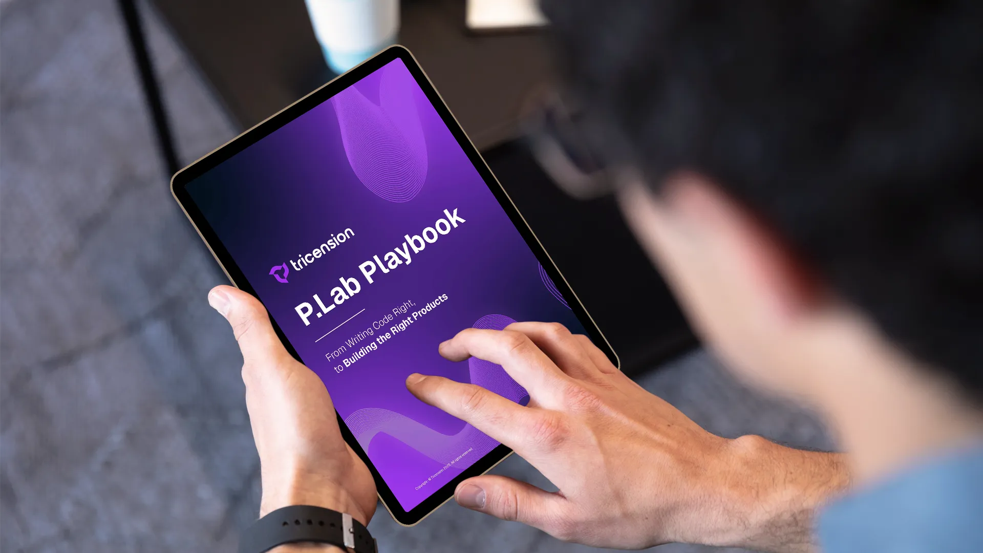 Person holding a tablet displaying a purple screen with the text 'P.Lab Playbook' and 'From Writing Code Right to Building the Right Products'.