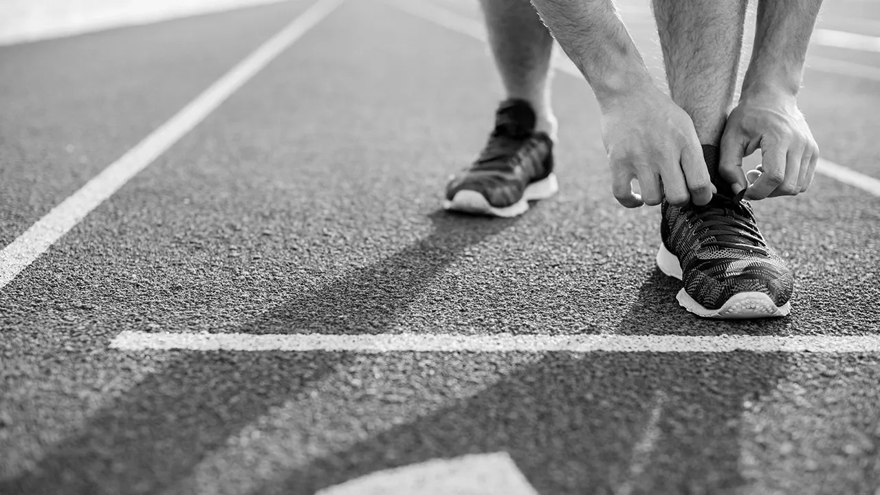 Athlete tying shoelaces on running shoes at the starting line of a track.