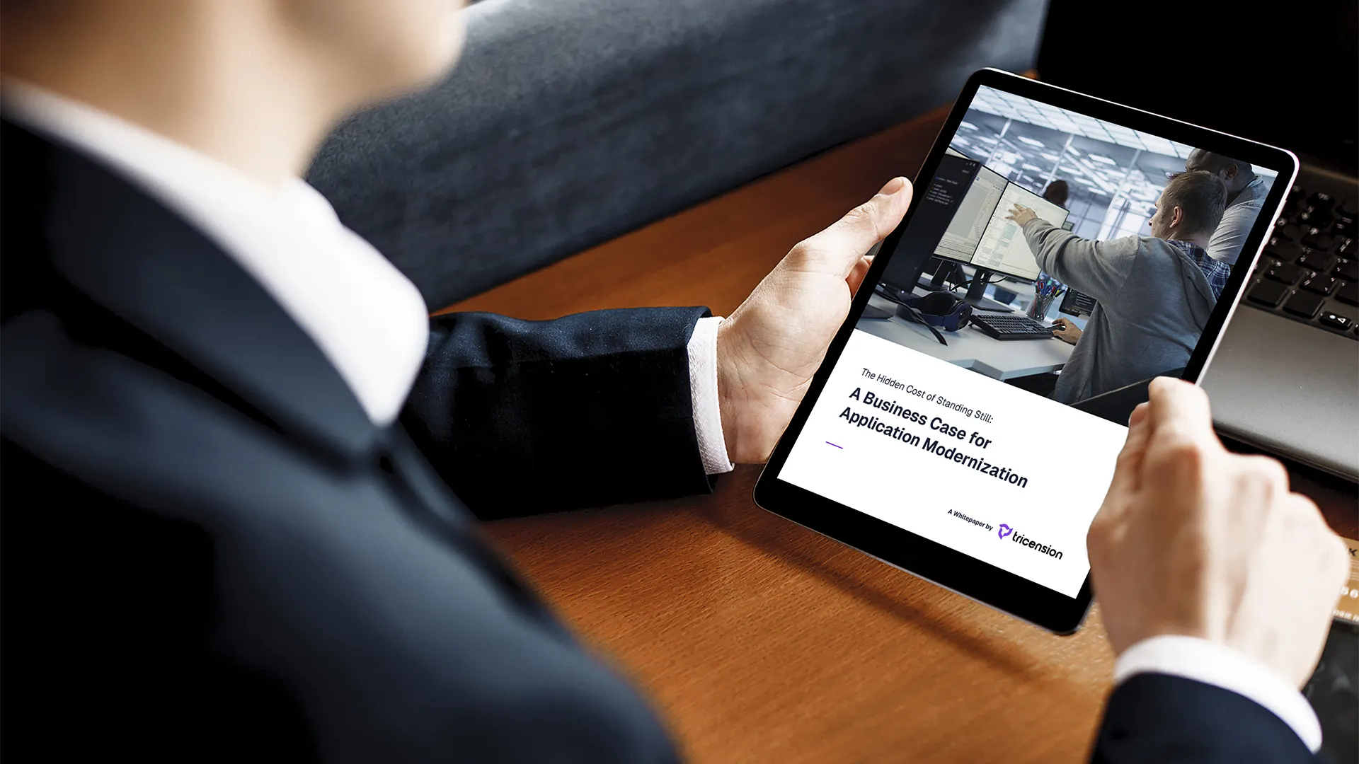 Person in a suit holding a tablet displaying a whitepaper titled 'A Business Case for Application Modernization' with an image of two people working at computer screens.