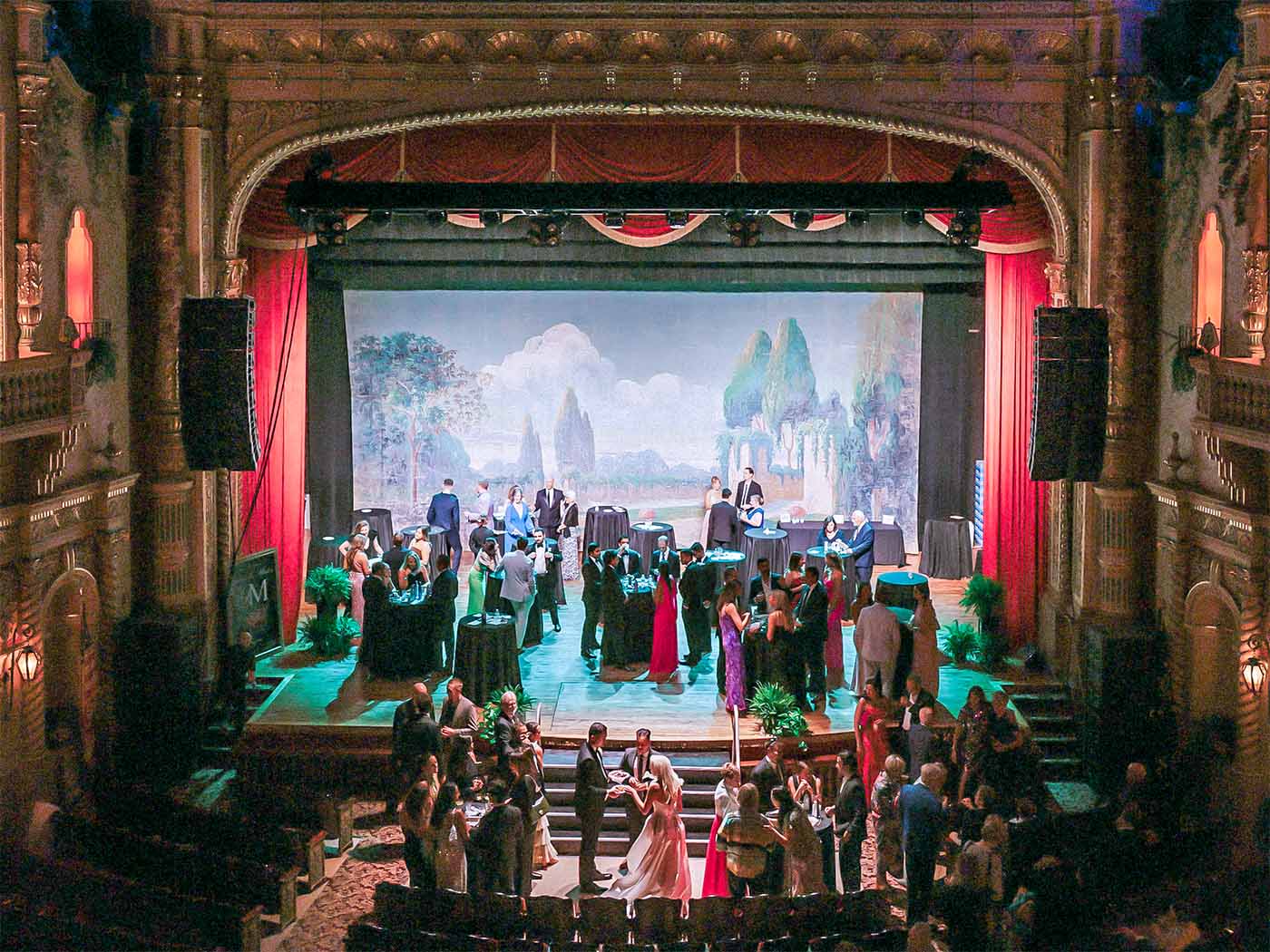 People dressed formally socializing at an elegant event with a painted backdrop on stage at The Paramount Theatre.