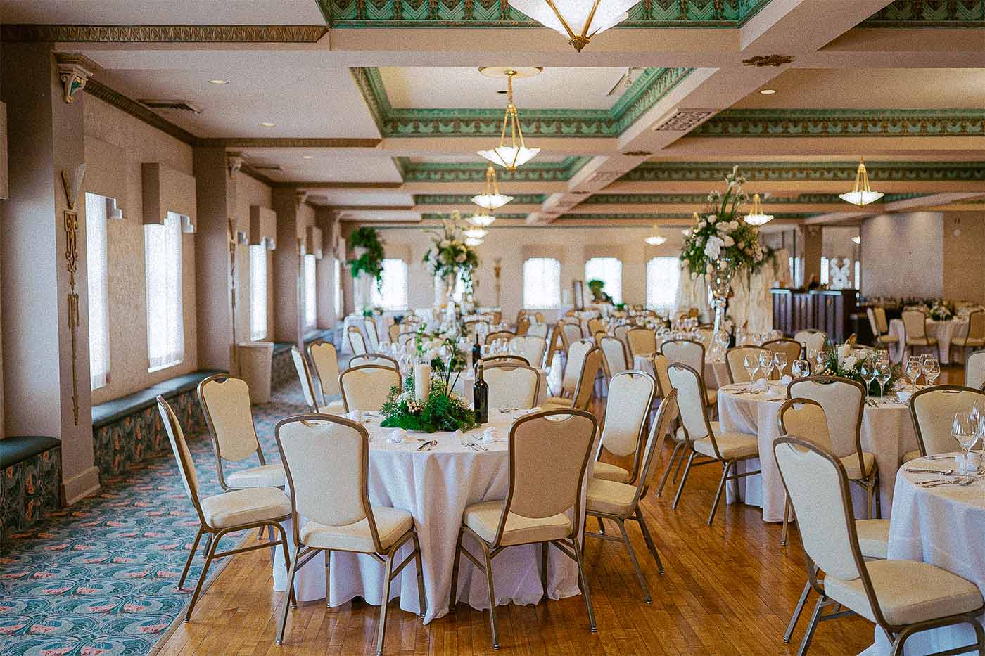 Elegant banquet hall with round tables covered in white tablecloths, beige chairs, floral centerpieces, and glassware set for a wedding reception in the Hardacre Ballroom at The Paramount Theatre