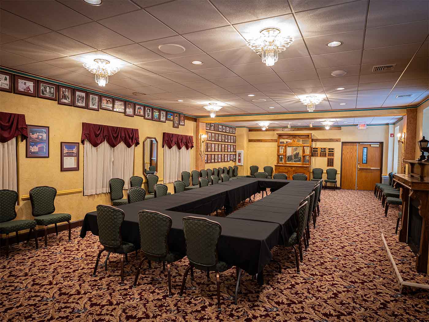 Formal conference room with U-shaped tables covered in black tablecloths, green patterned chairs, framed photographs on yellow walls, and ornate chandeliers at the Marquee Room at The Paramount Theatre.