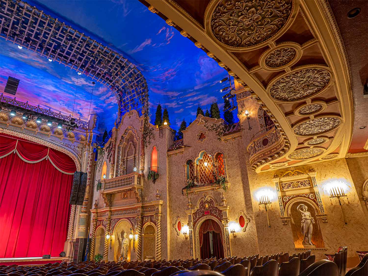 The Paramount Theatre interior with a decorated ceiling, red curtains on stage, classical statues, and rows of seats.