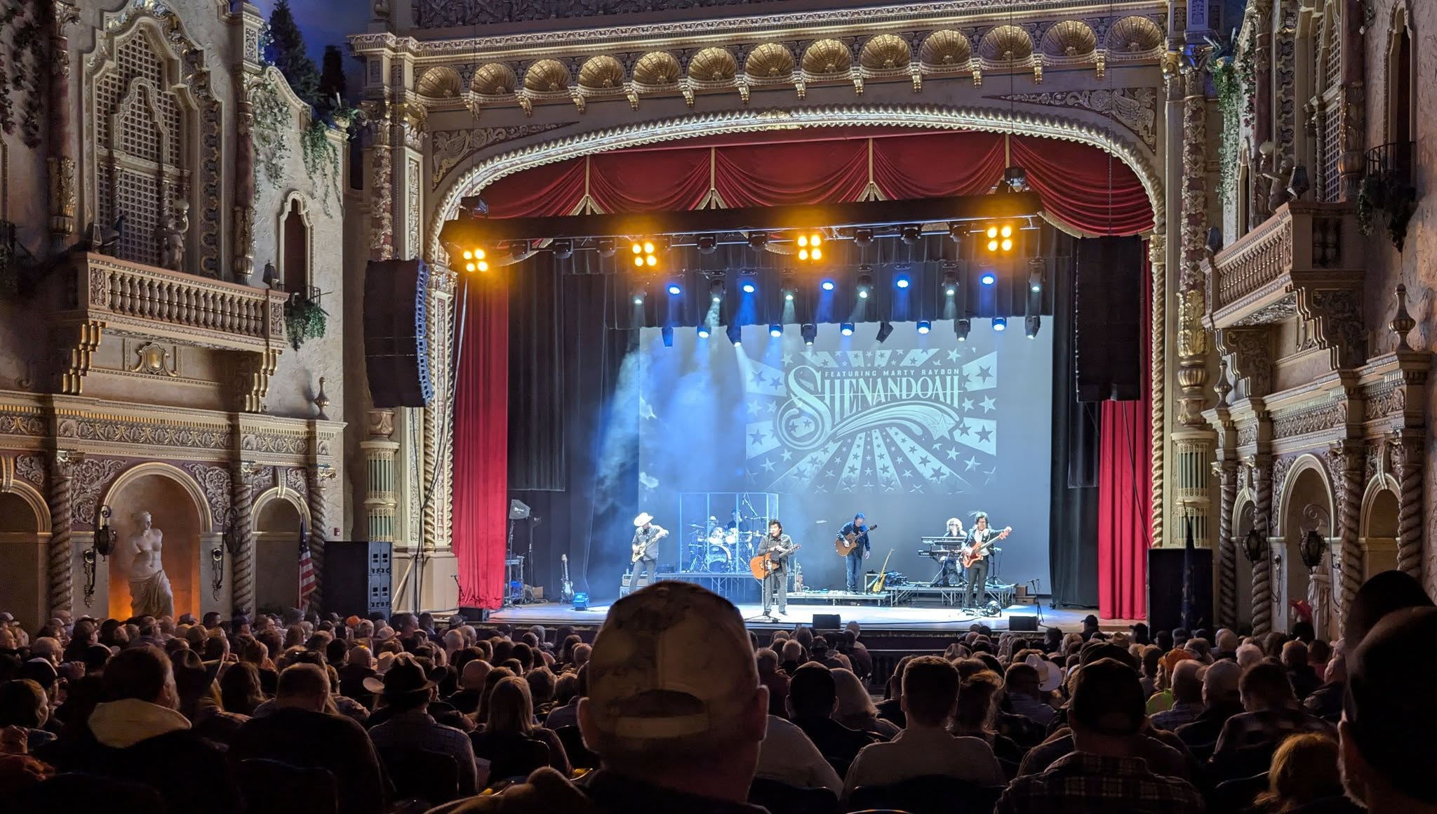 Live band performing on stage at The Paramount Theatre with audience watching, with Shenandoah logo projected behind.