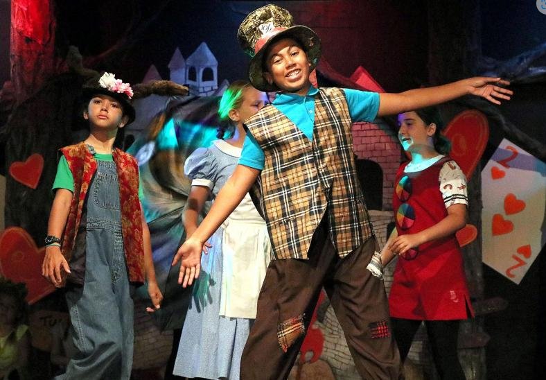Children in colorful costumes performing a stage play with a backdrop featuring playing cards and hearts during Summer Camps at The Paramount Theatre