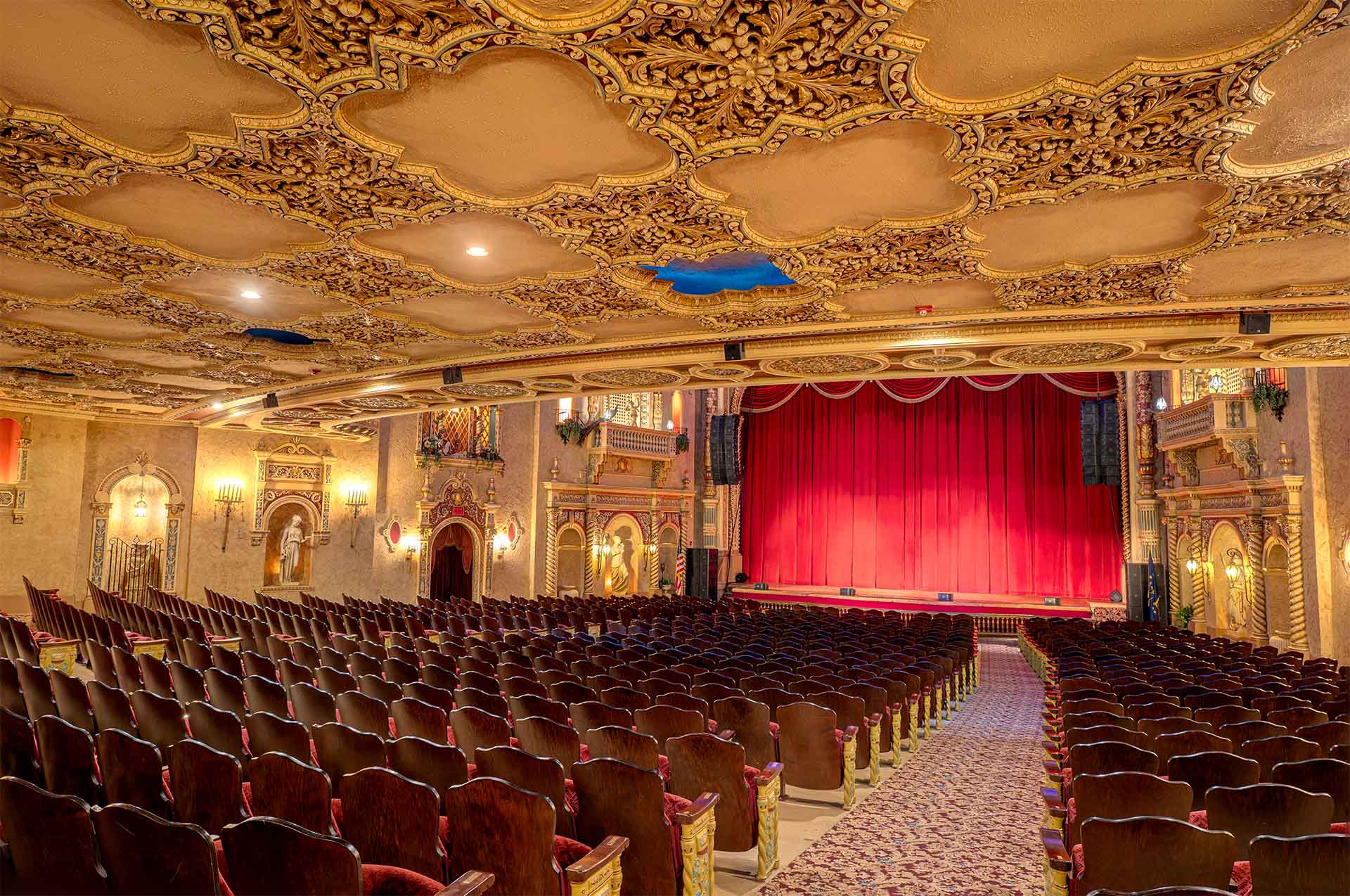 The Paramount Theatre auditorium with rows of wooden seats facing a stage with closed red curtains and an intricately decorated ceiling.