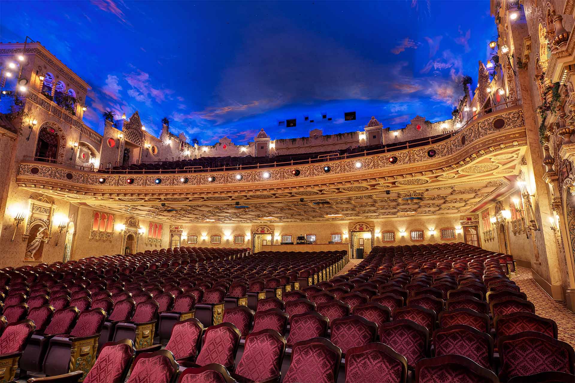 The Paramount Theatre auditorium with rows of red velvet seats, detailed gold trim, and a blue sky mural ceiling.
