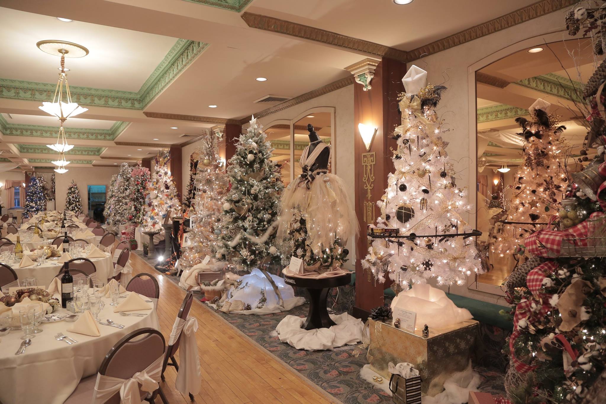 Elegant banquet hall with round tables set for dining and a row of creatively decorated Christmas trees, including one styled with a mannequin dressed in a tutu at The Paramount Theatre.