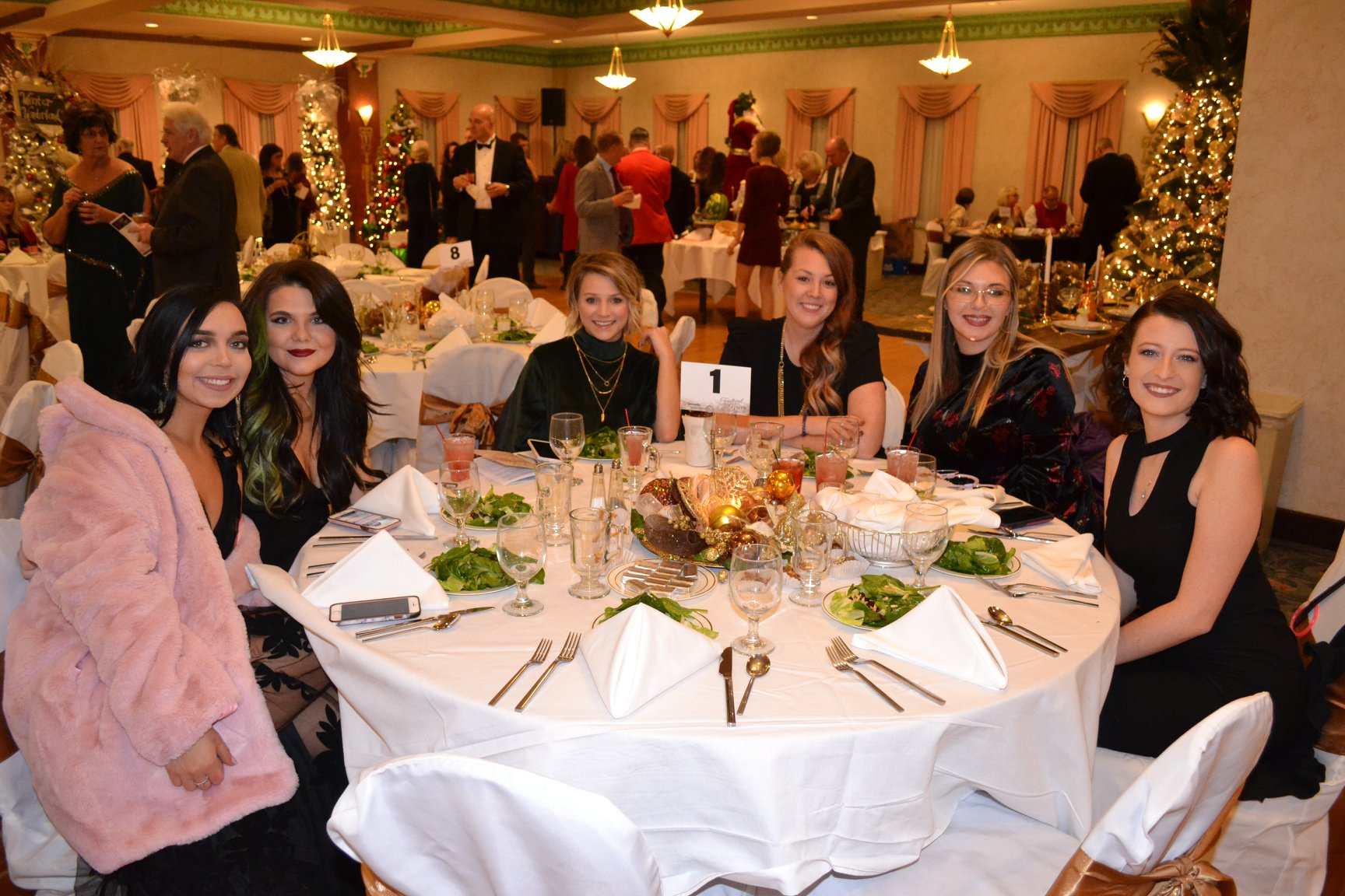 Six women dressed elegantly sitting around a decorated round table set with salads and drinks at the Festival of Trees Gala at The Paramount Theatre.