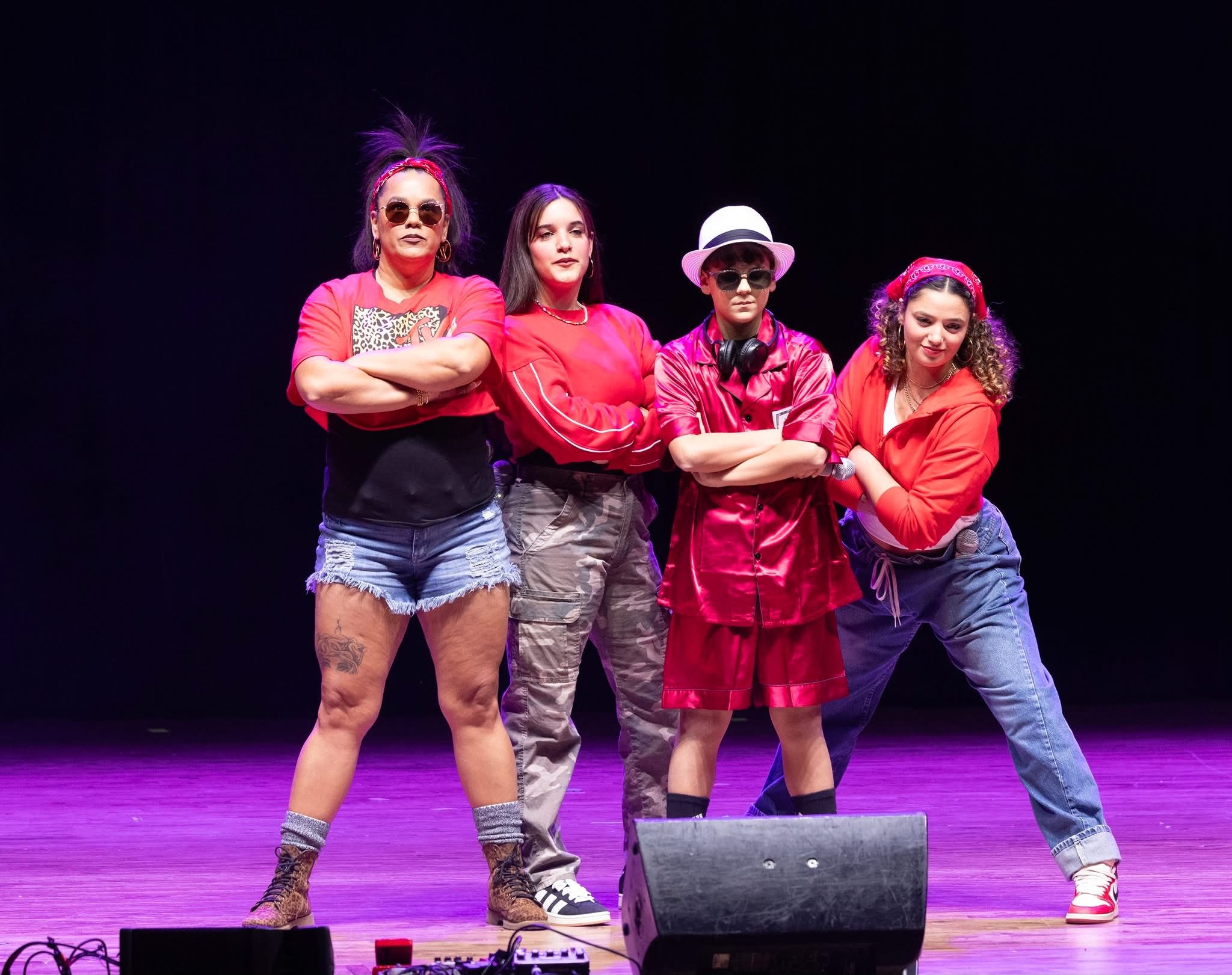 Four performers in casual red and denim outfits posing confidently on stage under purple lighting at the Lip Sync Battle at at The Paramount Theatre.