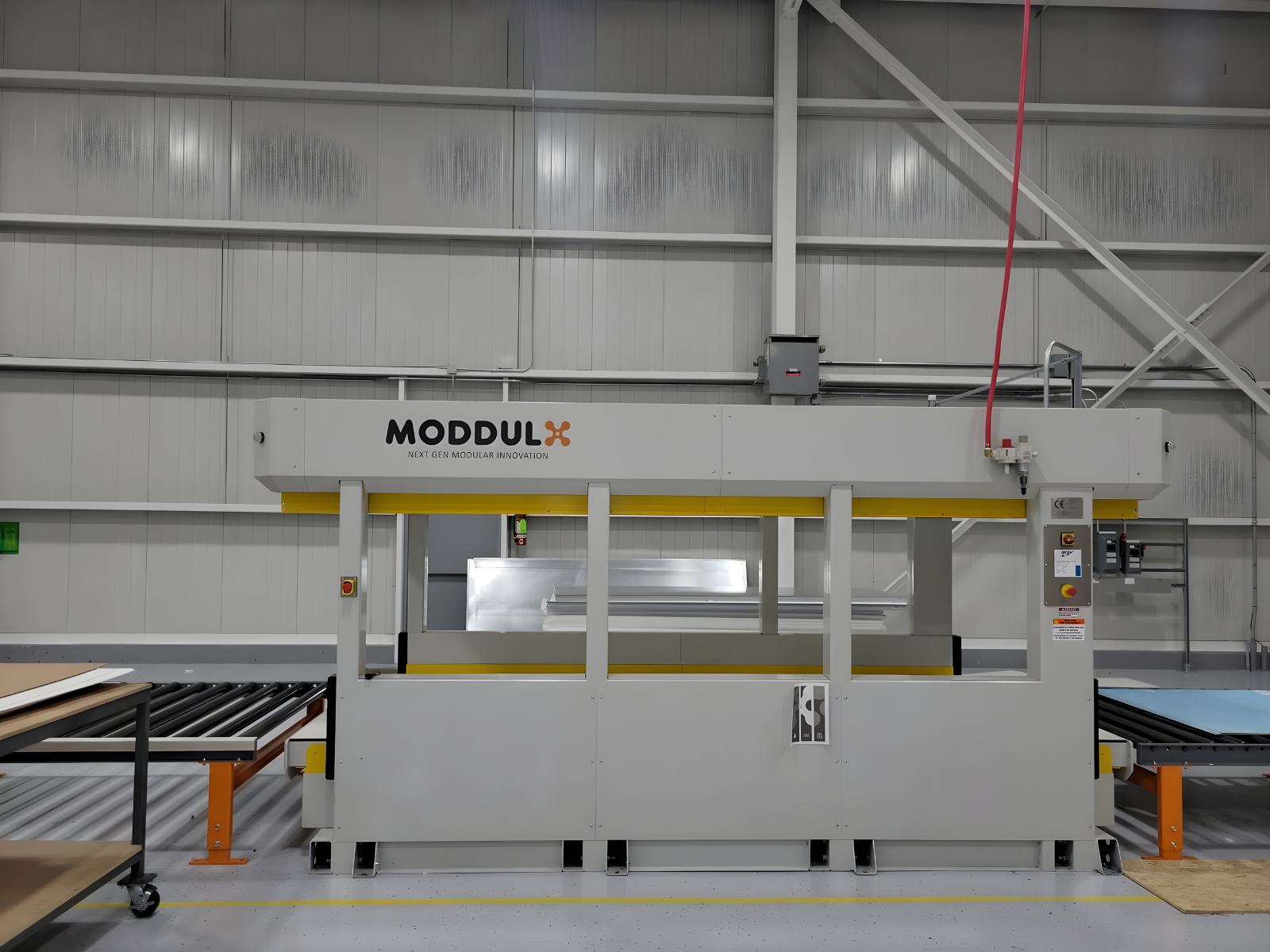 MODDULX branded industrial machine in a spacious factory setting with metal panels and conveyor rollers on each side.