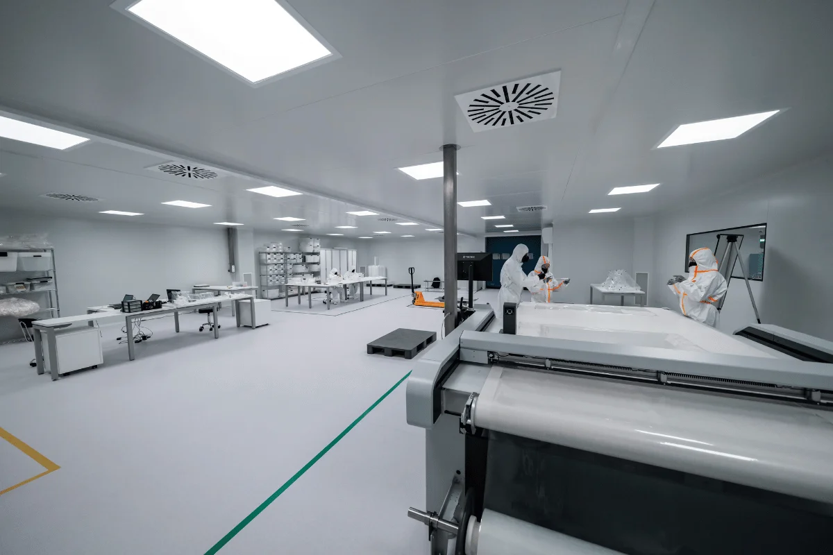 A modern laboratory with bright lighting, featuring scientists in protective gear working at clean tables and machinery.