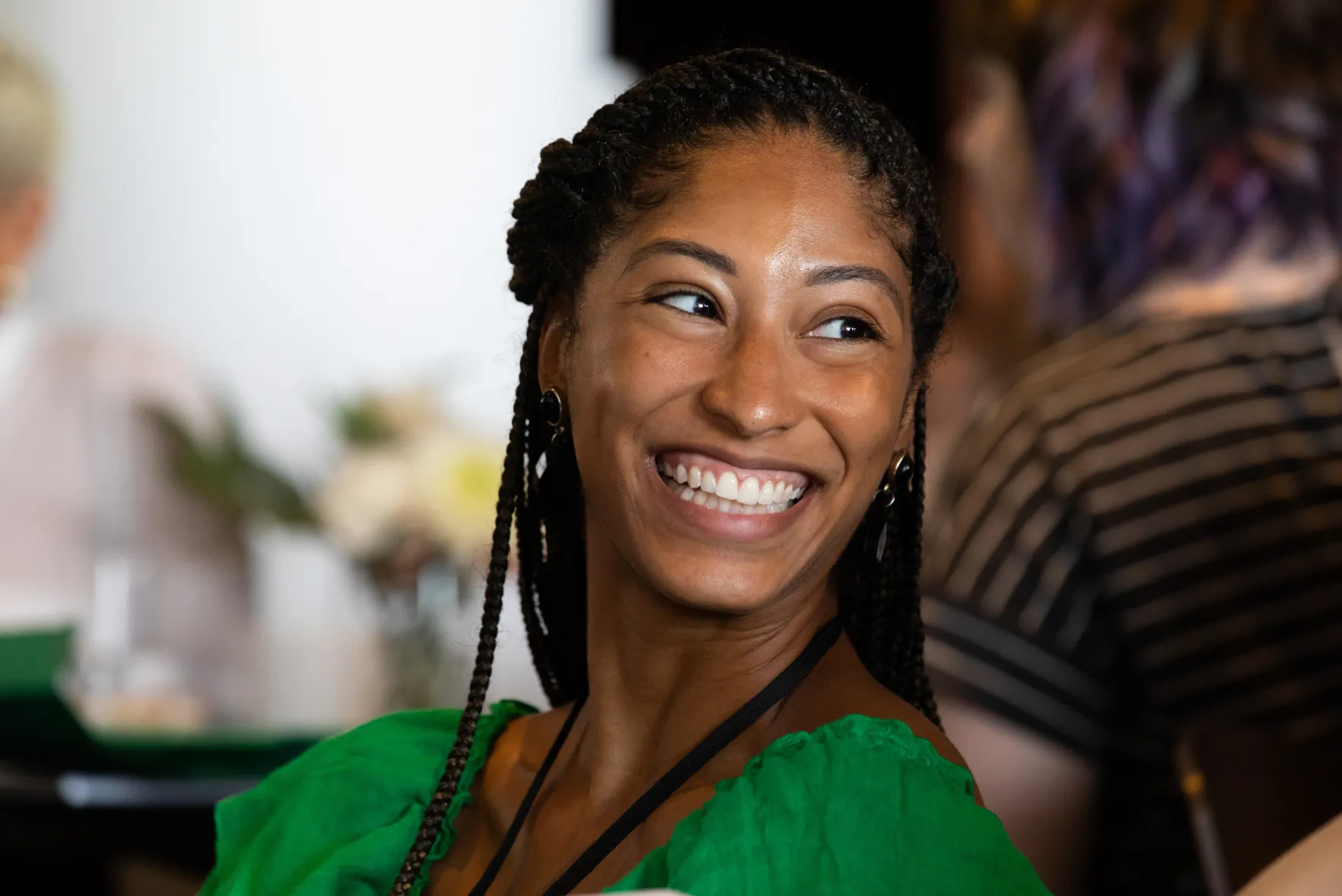 Smiling woman with braided hair wearing a green top looking to the side.