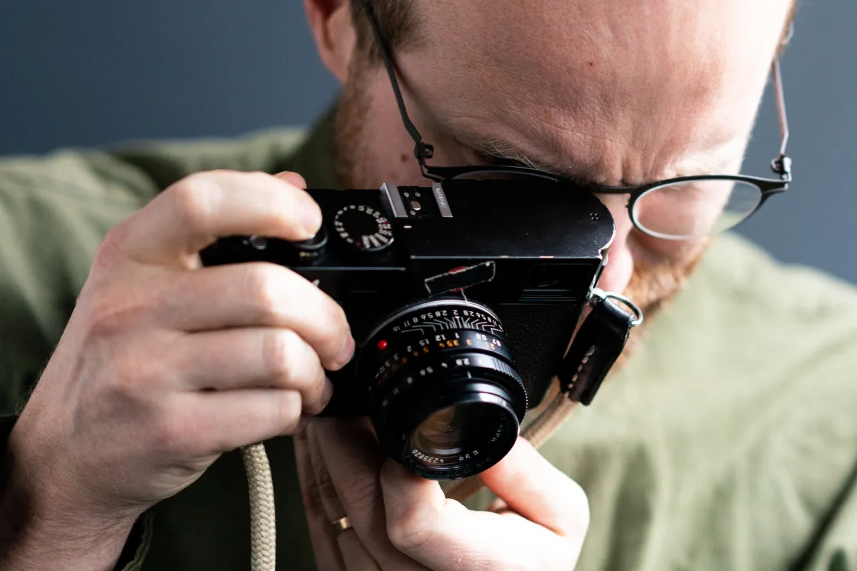 Man with glasses holding a black vintage camera close to his face, preparing to take a photo.