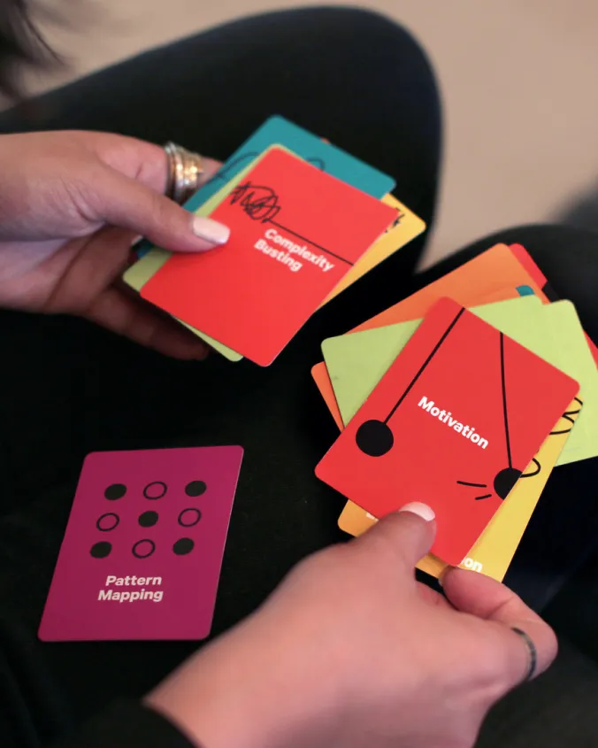 Person holding colorful cards with words like 'Complexity Busting', 'Motivation', and 'Pattern Mapping'.