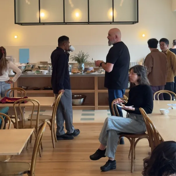 People socializing and eating in a modern cafe with wooden floors and chairs.