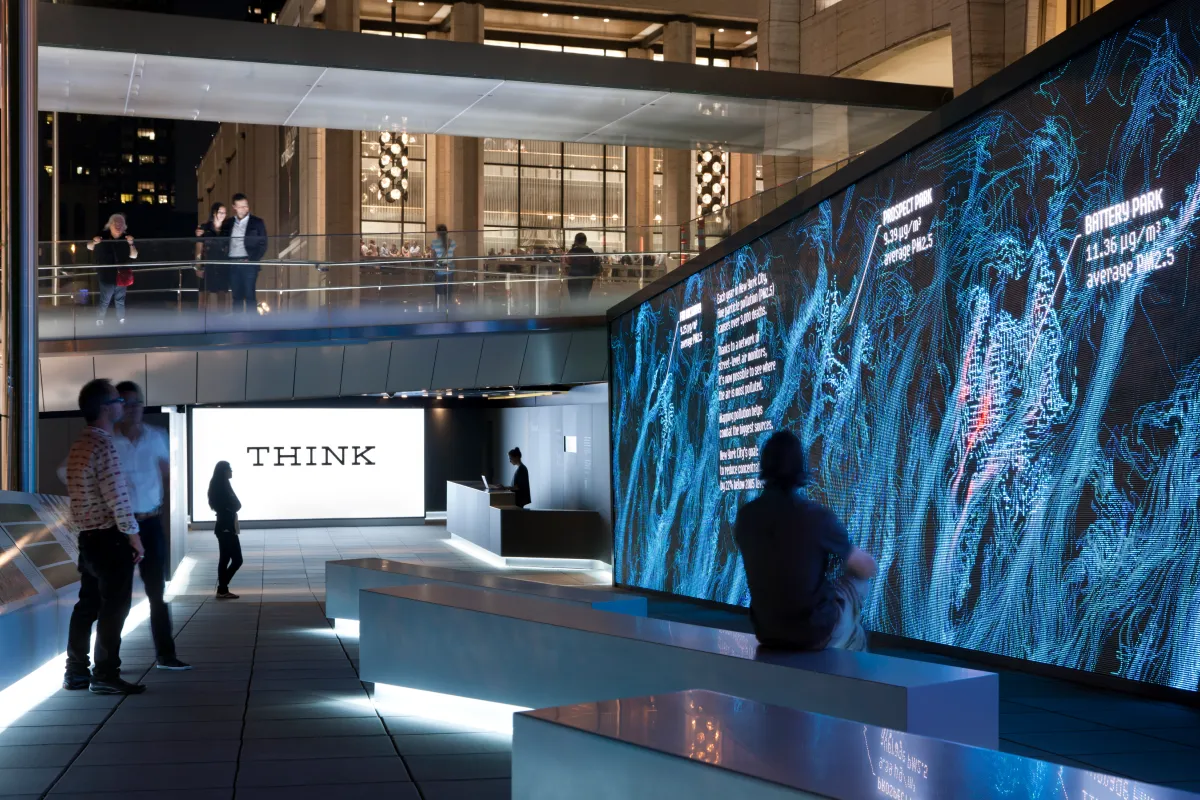 People in a modern indoor space with a large digital wall displaying blue abstract data visuals and a bright screen with the word THINK.