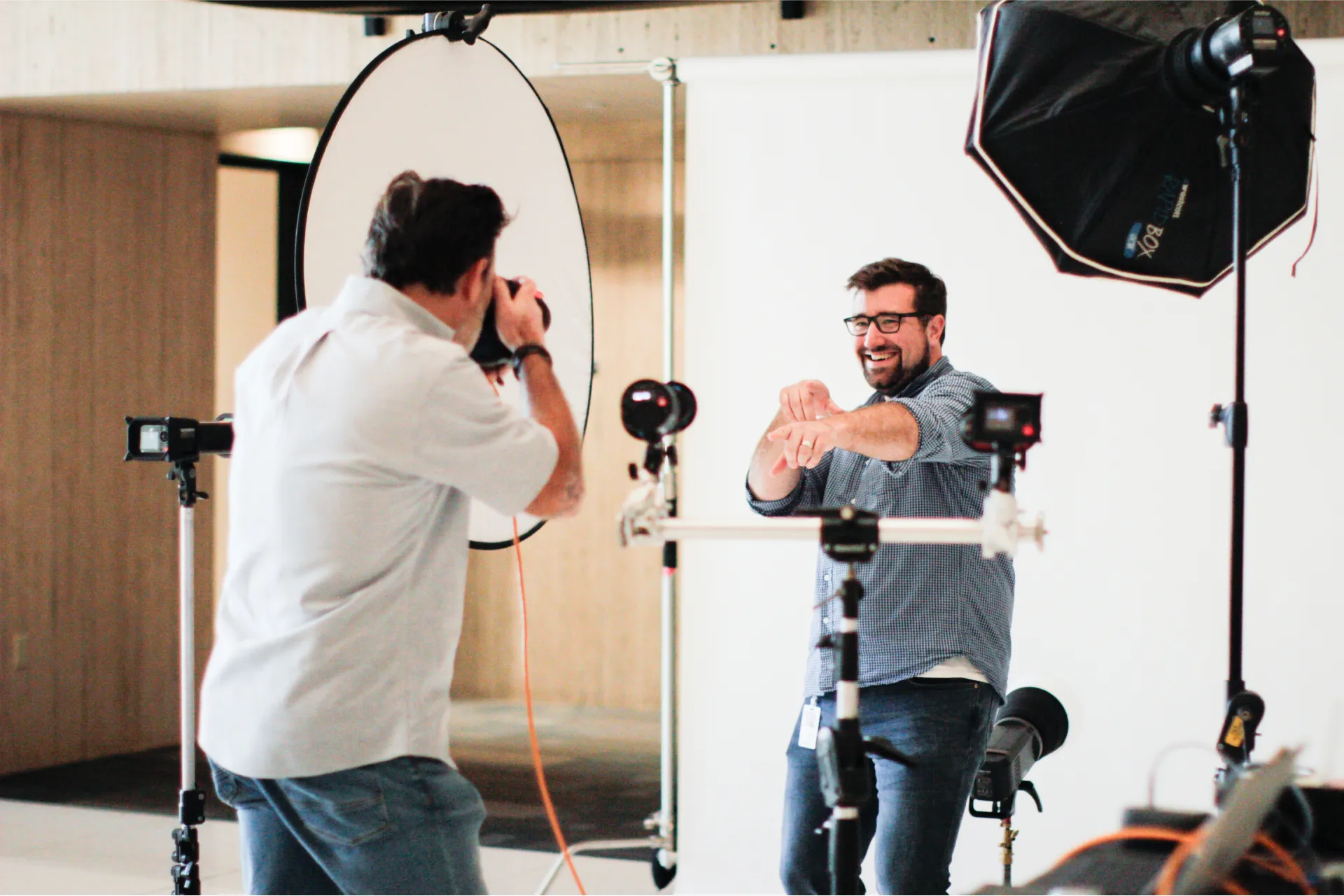 Photographer taking pictures of a smiling man posing in a studio with professional lighting equipment.