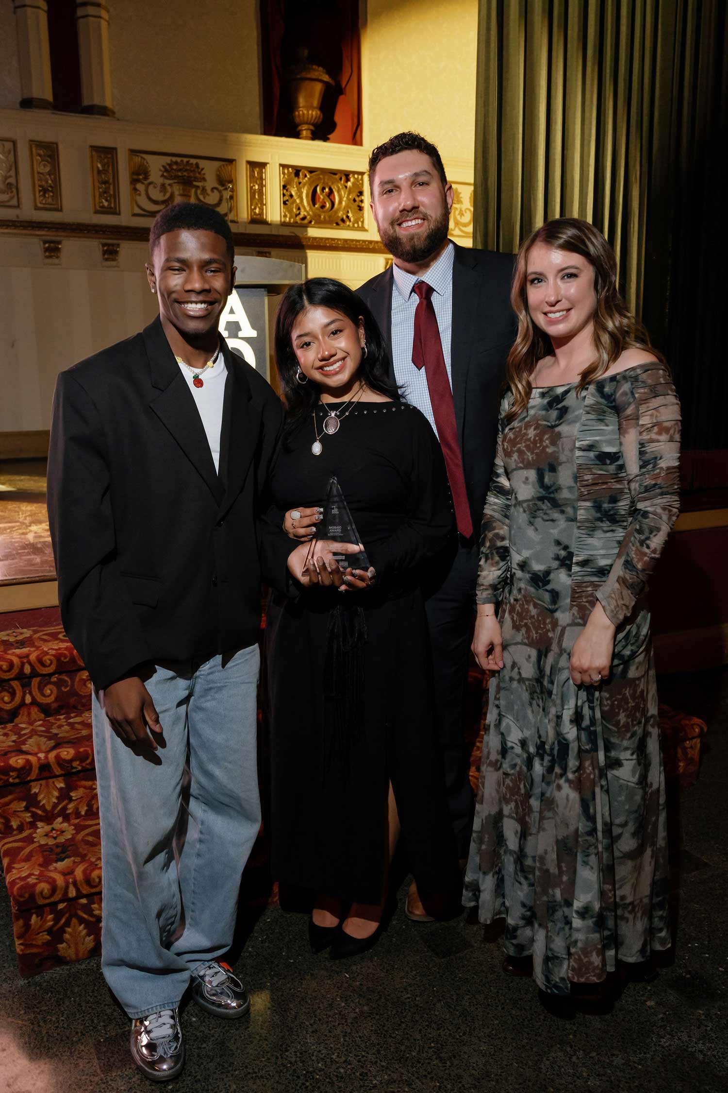 Four people smiling at an award event, with one woman in the center holding a glass trophy.