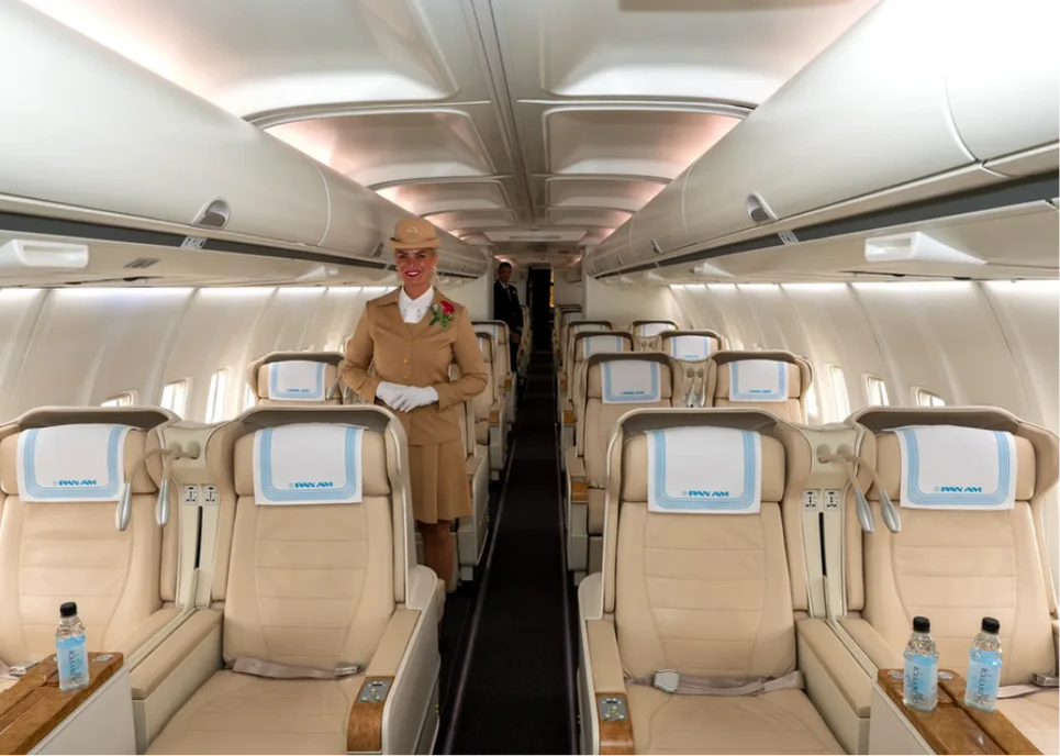 Pan Am flight attendant stands in a cabin of cream leather seats, ready to welcome guests aboard the private jet.