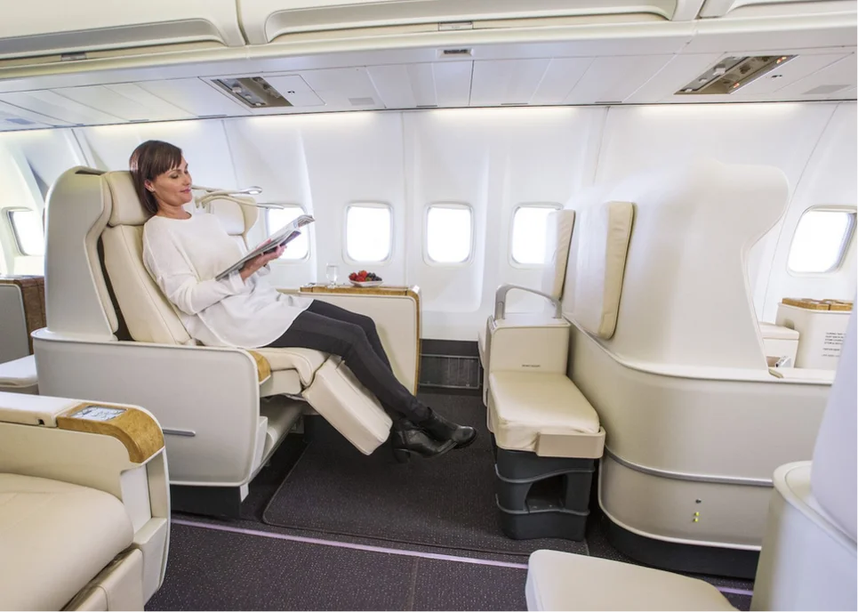 Passenger relaxes in a reclining Pan Am seat, reading under soft cabin light designed for long-haul comfort.