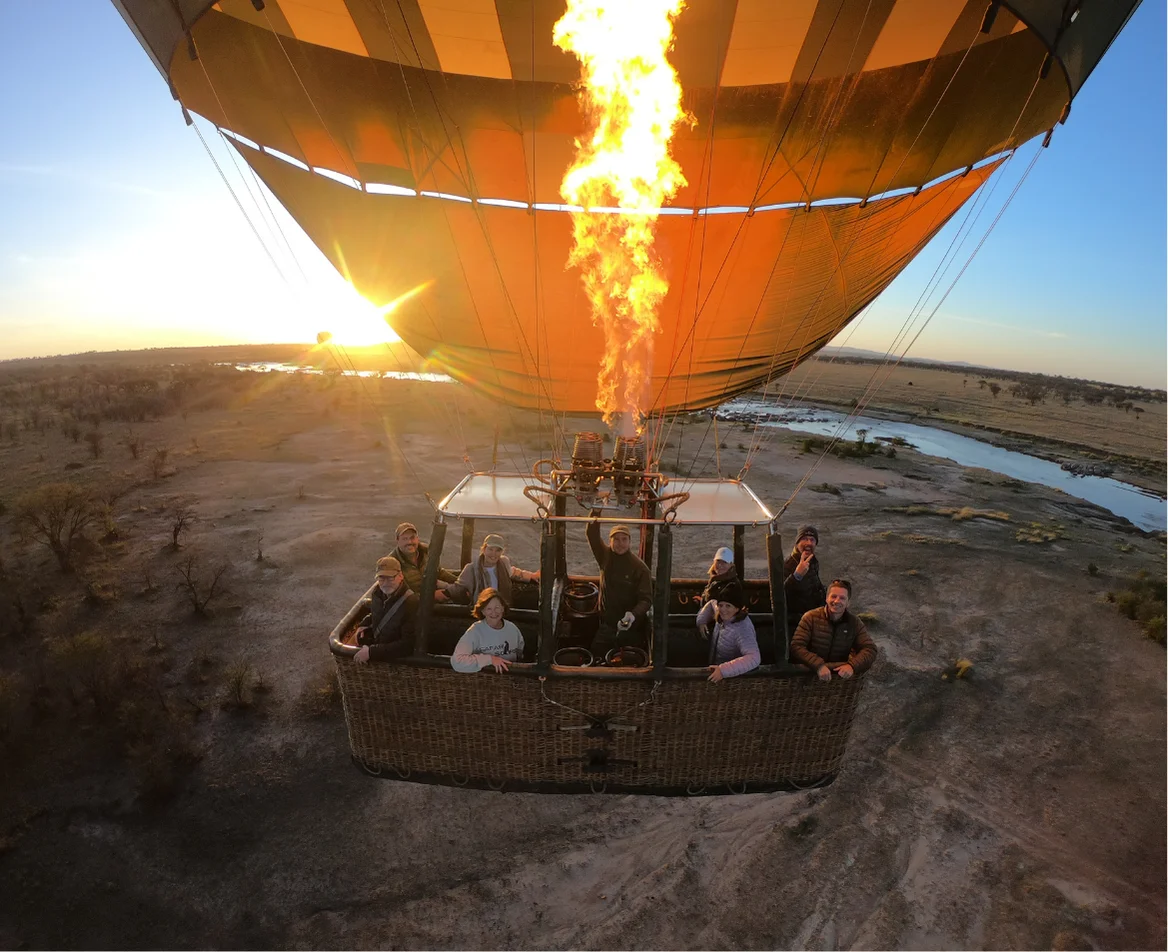 A hot air balloon rises over the Serengeti plains at sunrise, offering sweeping views of the African landscape.