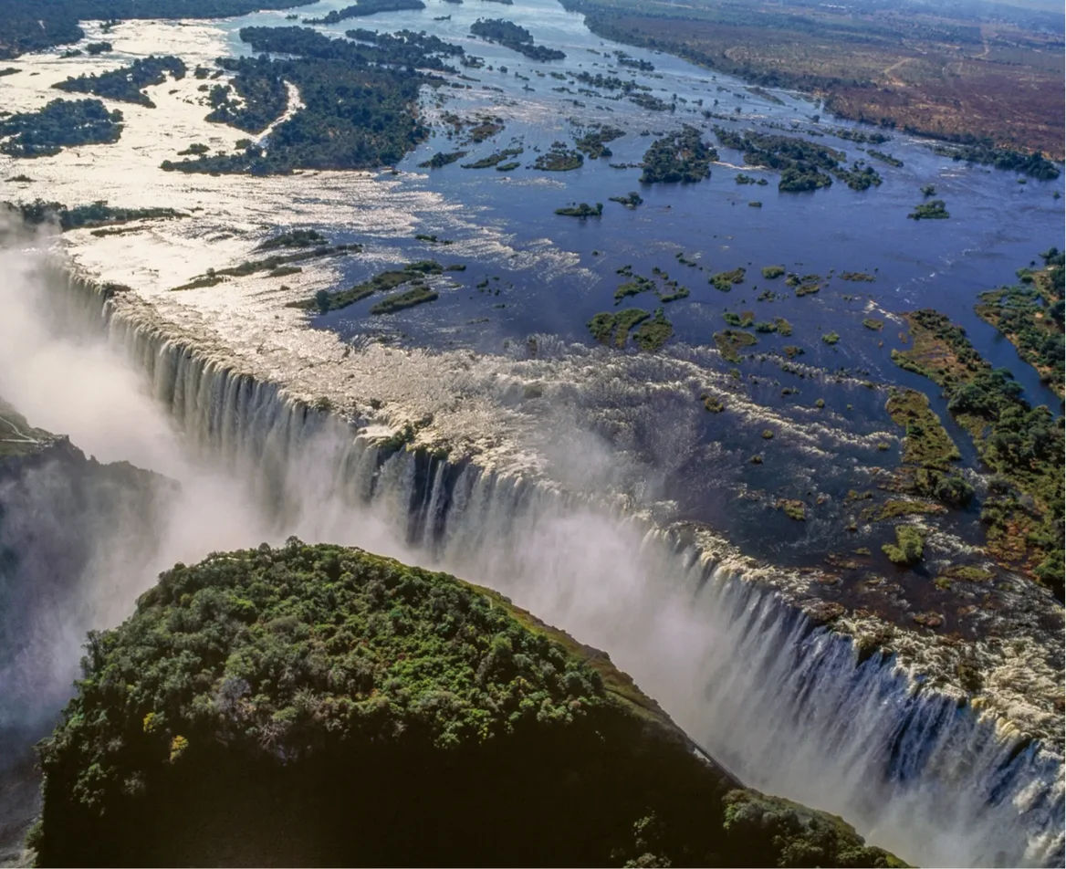 An aerial view of Victoria Falls with mist rising from the cascading water along the Zambezi River.
