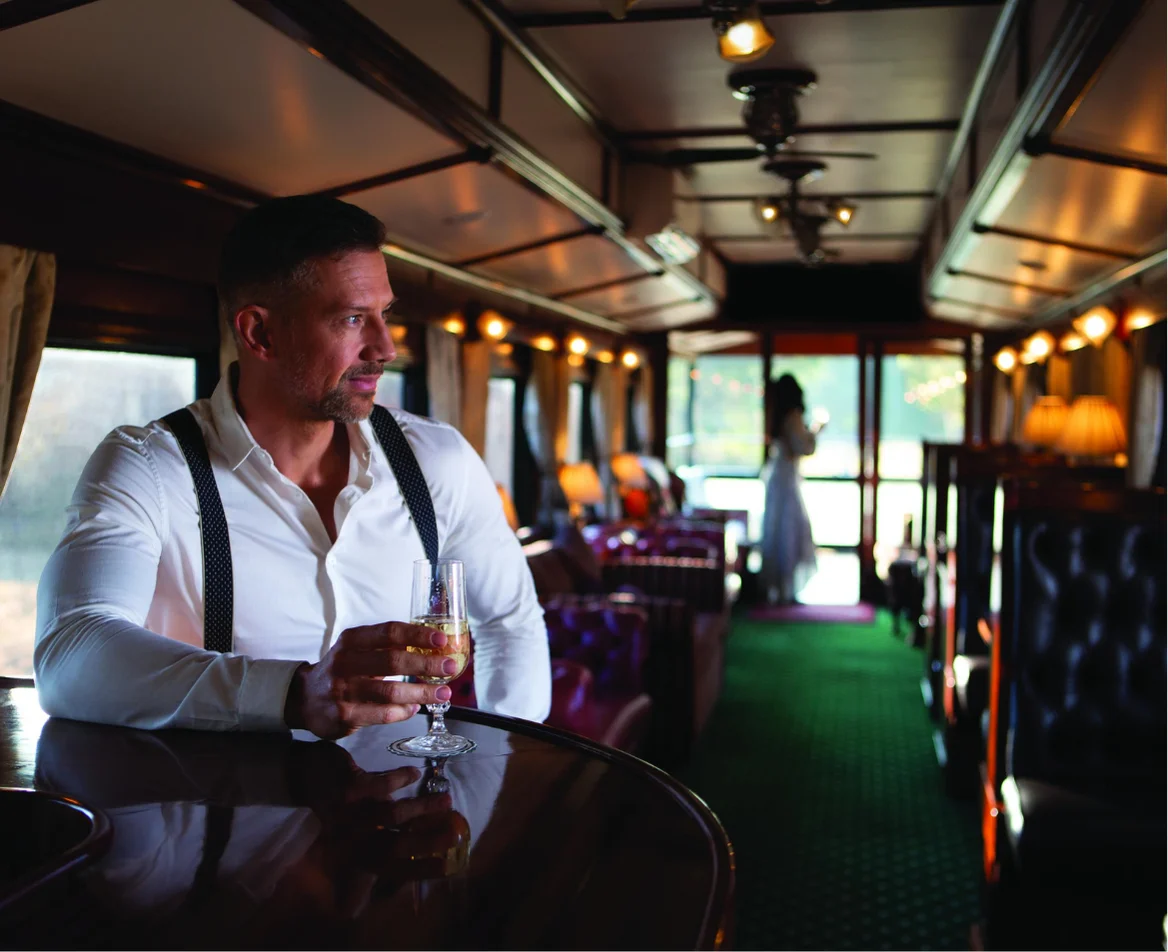 A traveler enjoys champagne in a vintage lounge car aboard Rovos Rail, evoking the romance of classic train travel.